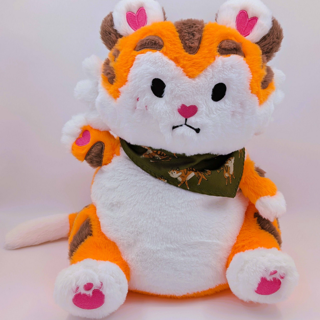Plush toy tiger with an orange and white body, brown accents, and a green bandana on a light pink background.