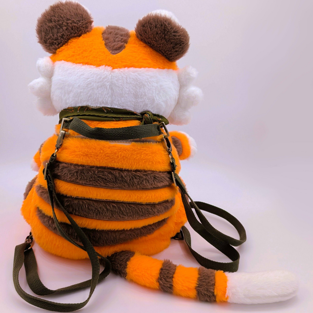Back view of a plush backpack tiger with an orange and white body, brown accents, and a green bandana on a light background.