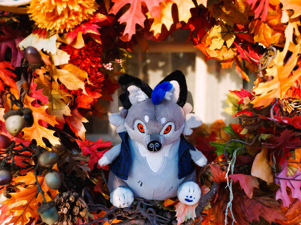 Plush toy of Wolfgang the werewolf with blue hair and a blue denim vest surrounded by fall leaves