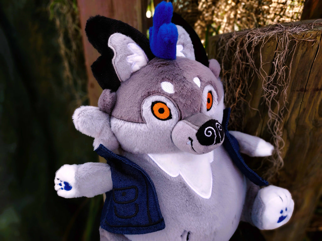 Plush toy of Wolfgang the werewolf with blue hair and a blue denim vest next to a log