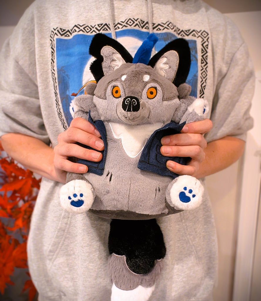 Plush toy of Wolfgang the werewolf with blue hair and a blue denim vest being held by a person wearing a hoodie with a full moon