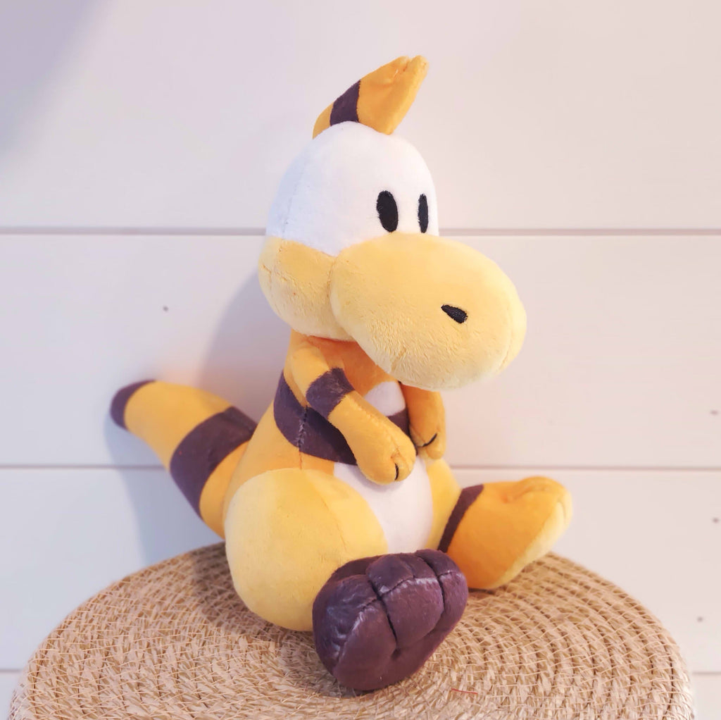 Yellow plush toy of Zid the yellow dinosaur with a brown foot and brown striped tail