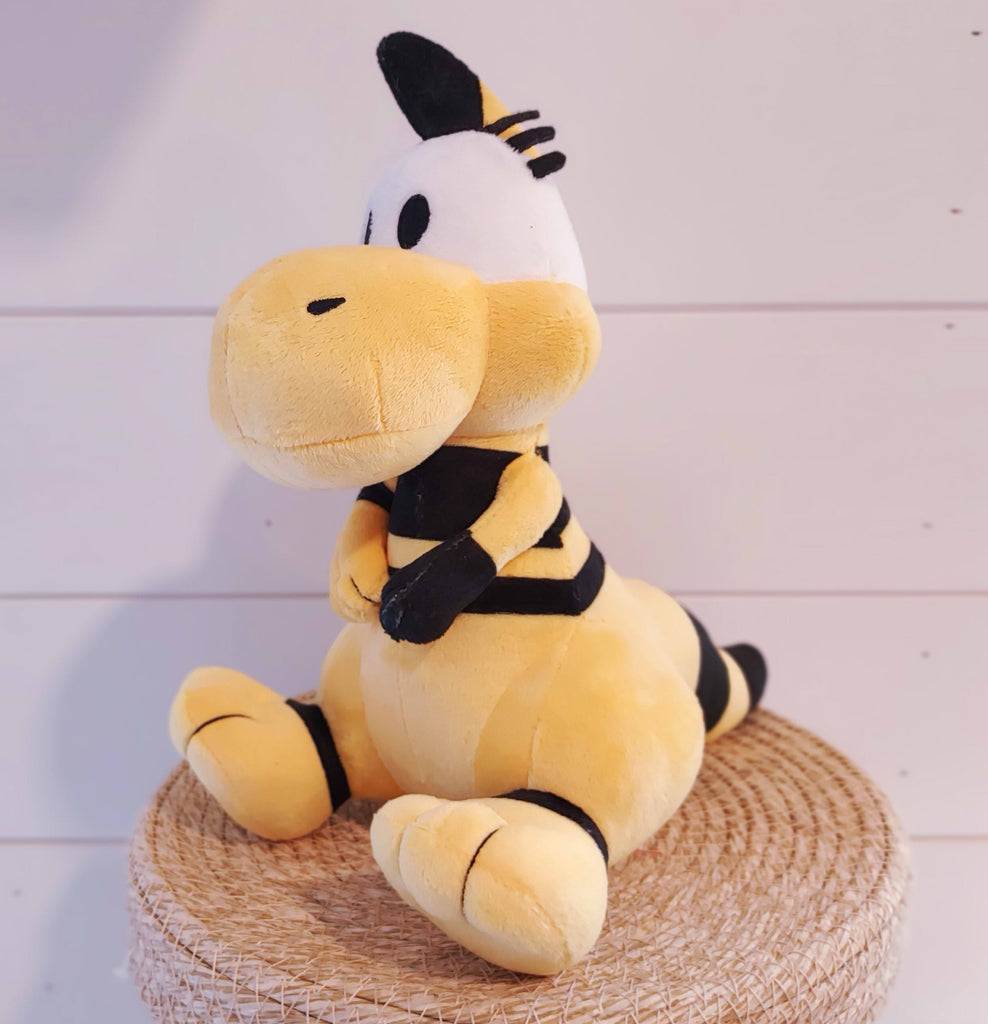 Plush toy of Zniw the yellow female dinosaur with black striped tail and big eyelashes