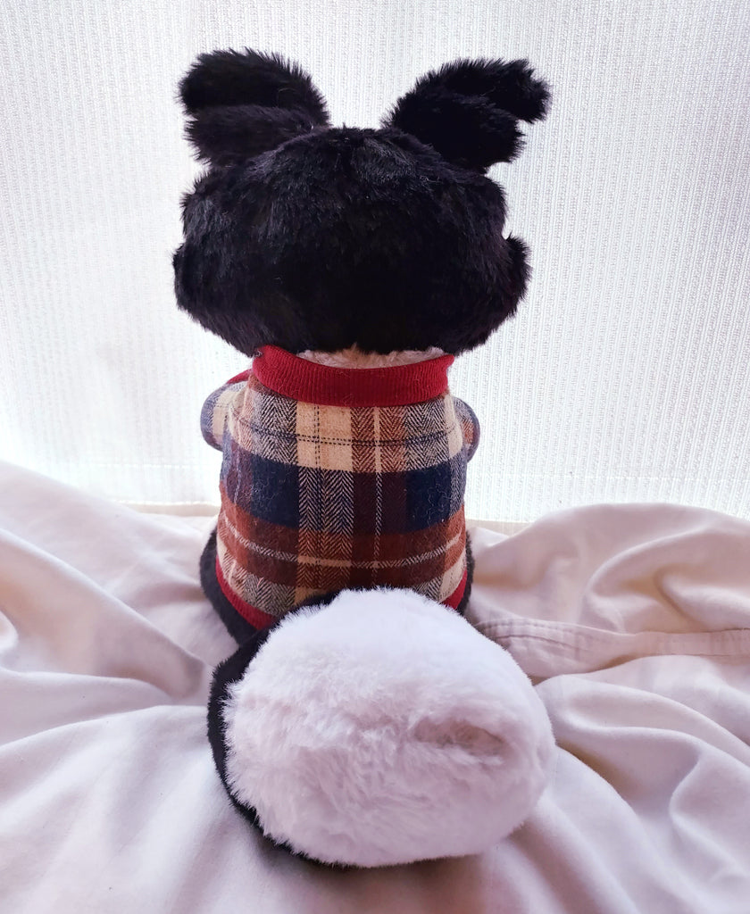 Back view of a plush toy of a black and white border collie wearing a red, beige, and blue plaid sweater
