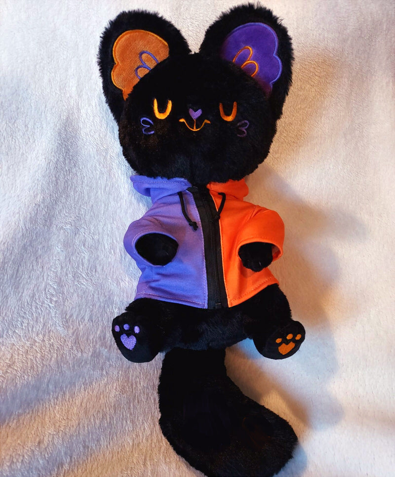 Plush toy of Pumpkin Purr the black Halloween cat. She has purple and orange ears and a purple and orange hoodie