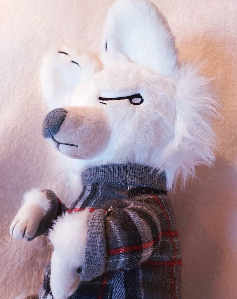 Closeup of a plush toy of Anxiety Fox, a white fox wearing a grey and red plaid sweater