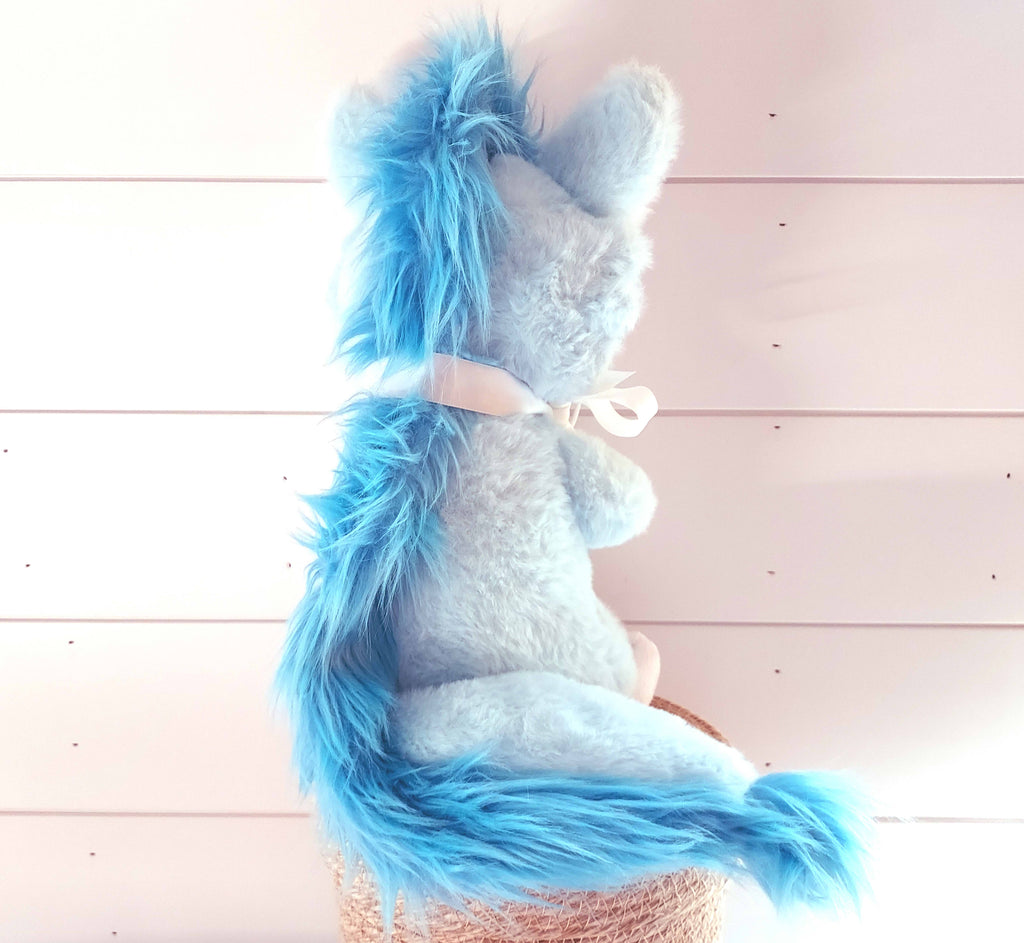 Back view of a plush toy of Cloud the blue dragon wearing a white ribbon