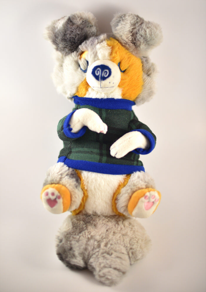 Plush toy of an Australian shepherd wearing a green and blue plaid sweater